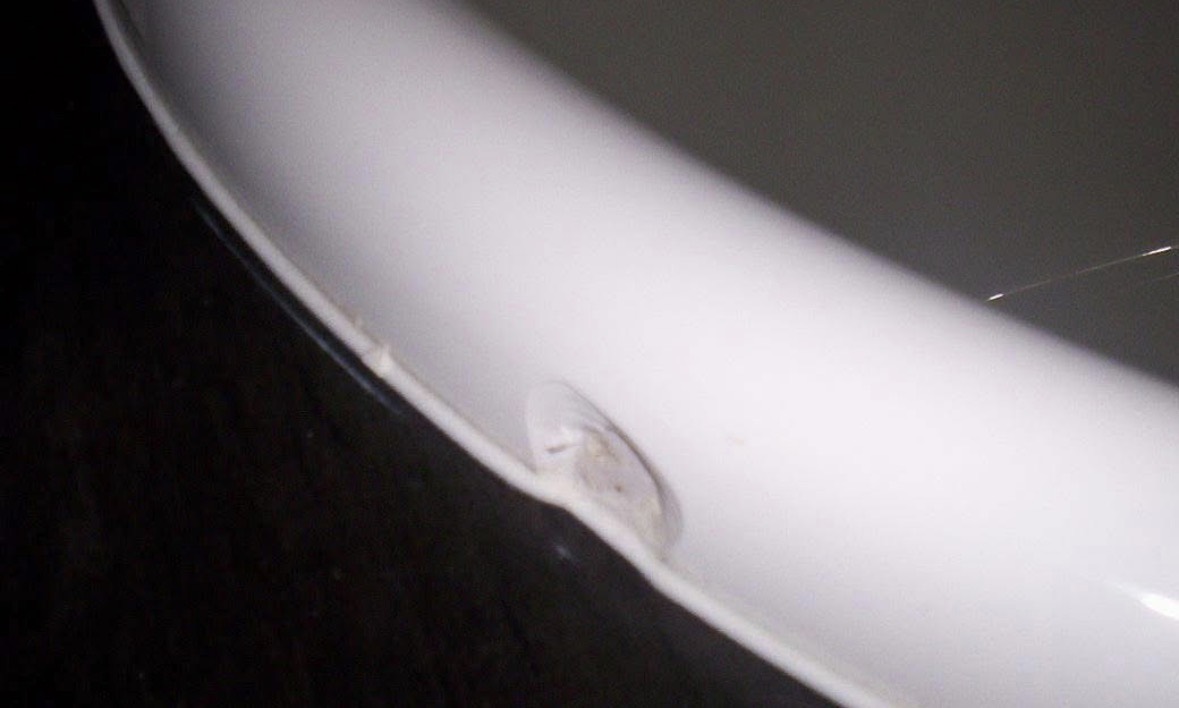 The curved white lip of a bath against a dark floor, with a chip broken through the glossy surface near the edge.