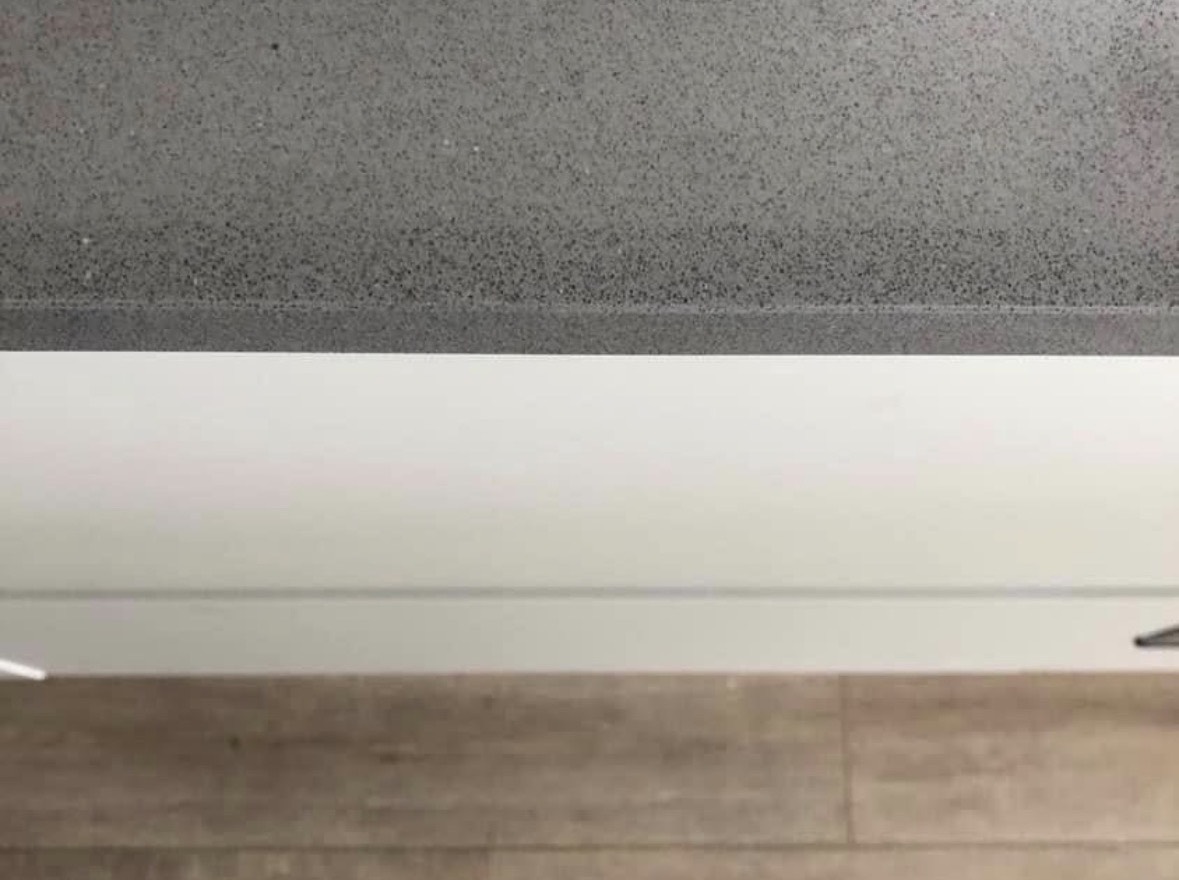 The same speckled stone benchtop after repair, the dark edge band running clean and unbroken.