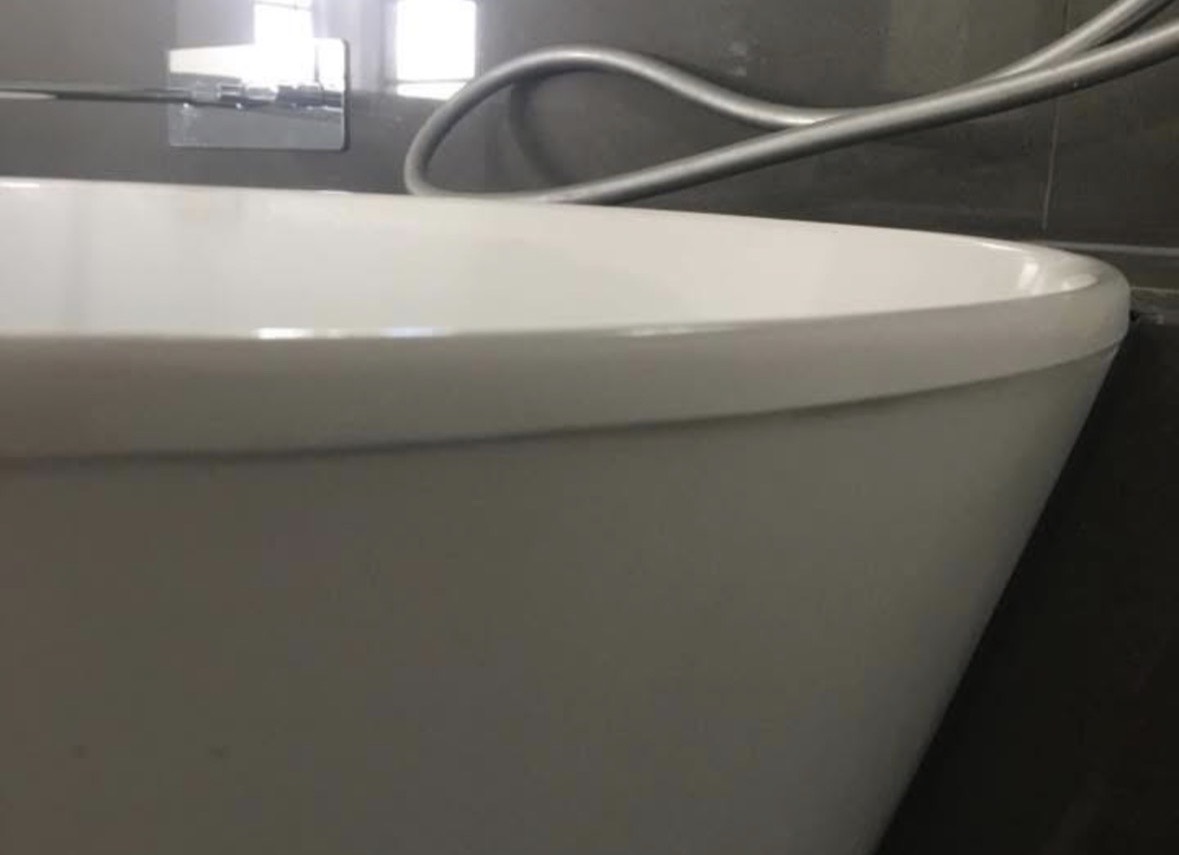 The same freestanding bath after repair, the rim smooth and white against dark stone wall tiles, with the chip gone.