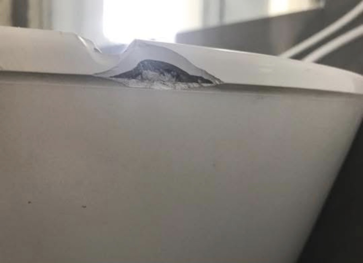 The rim of a white freestanding bath with a chip broken through the glossy surface, exposing the dark grey material underneath.
