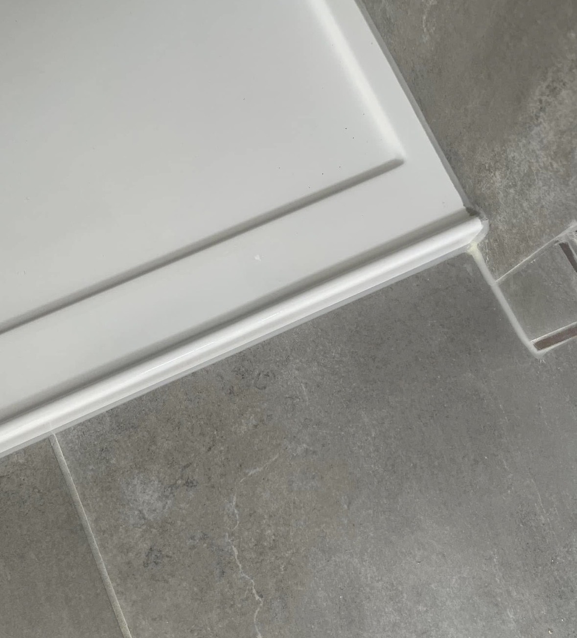 The same shower base corner after repair, the moulded edge continuous and white with no sign of the chip.
