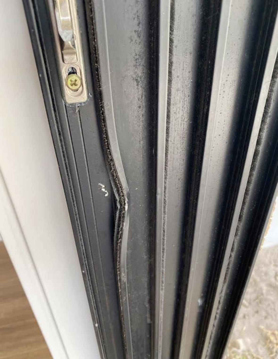A black aluminium sliding door frame with a visible dent kinking the straight line of the frame.