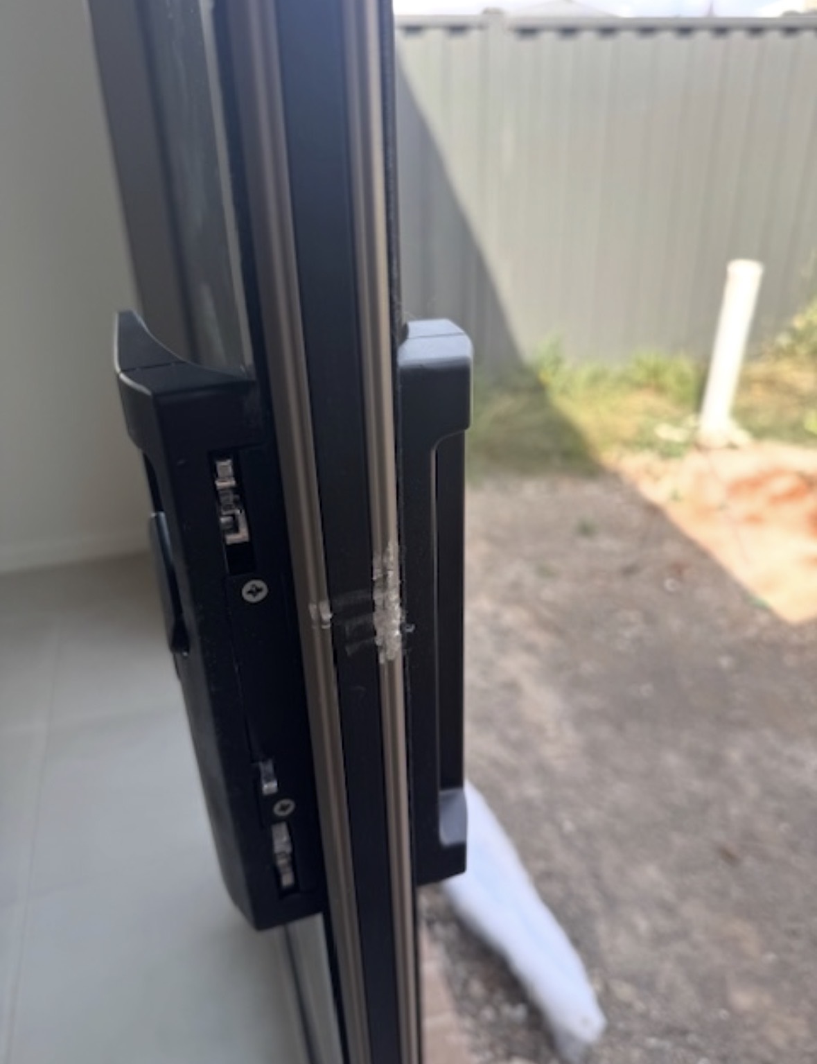 The outer track side of a black aluminium sliding door frame with damage and filler visible along the edge.