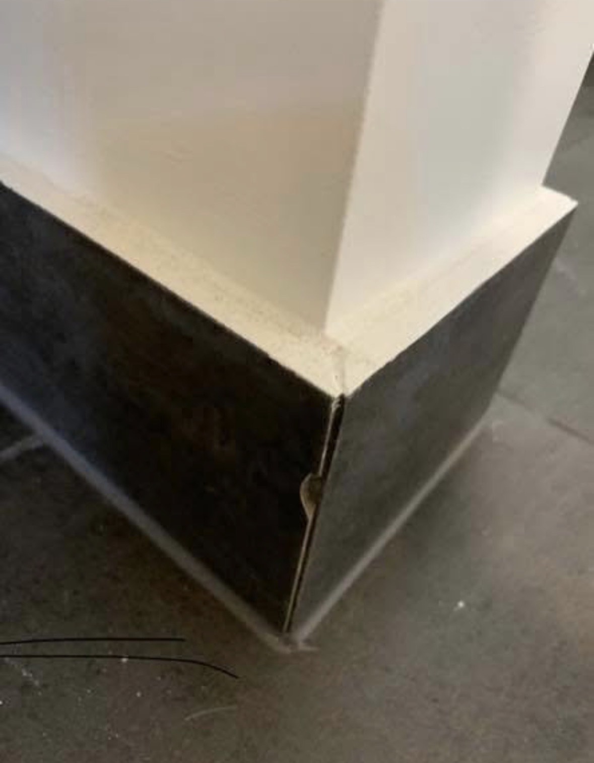 The corner of a dark tiled surface below a white benchtop overhang, with a visible chip and split along the edge where two tiles meet.