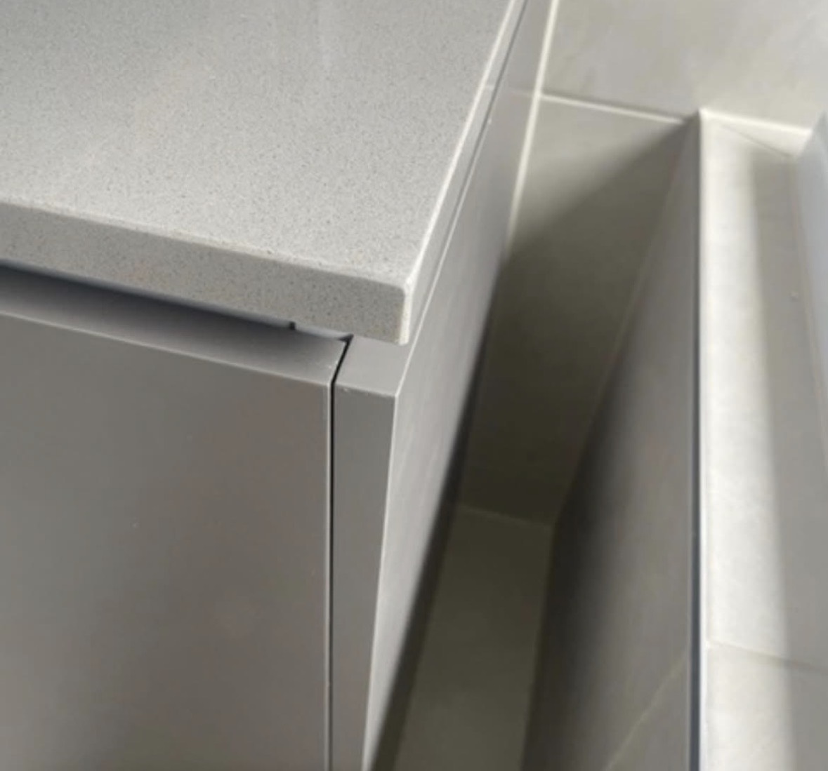 The same grey stone vanity corner after repair, the front edge running straight and unbroken with the speckled finish continuing through where the chip was.