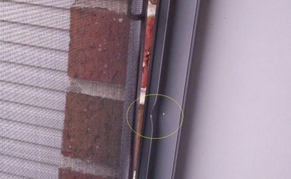 An aluminium window frame beside brickwork and a flyscreen, with a yellow circle drawn around a dented section of the frame.